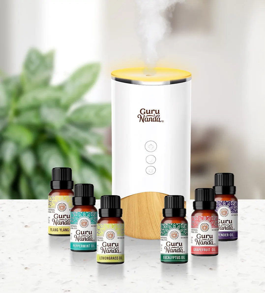 A GuruNanda diffuser releasing mist behind a row of essential oil bottles