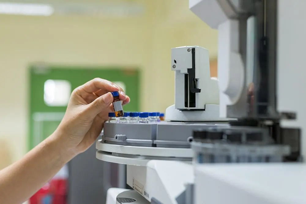 A hand loading a sample vial into a GC-MS machine